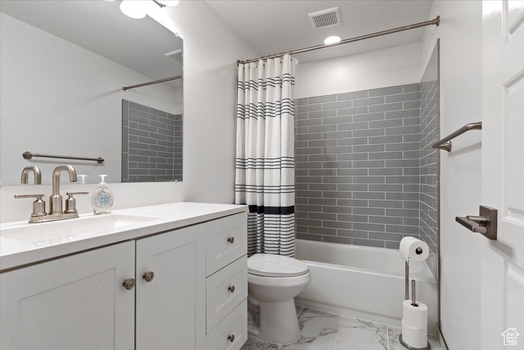 Full bath featuring toilet, vanity, marble look tile flooring, and shower / tub combo