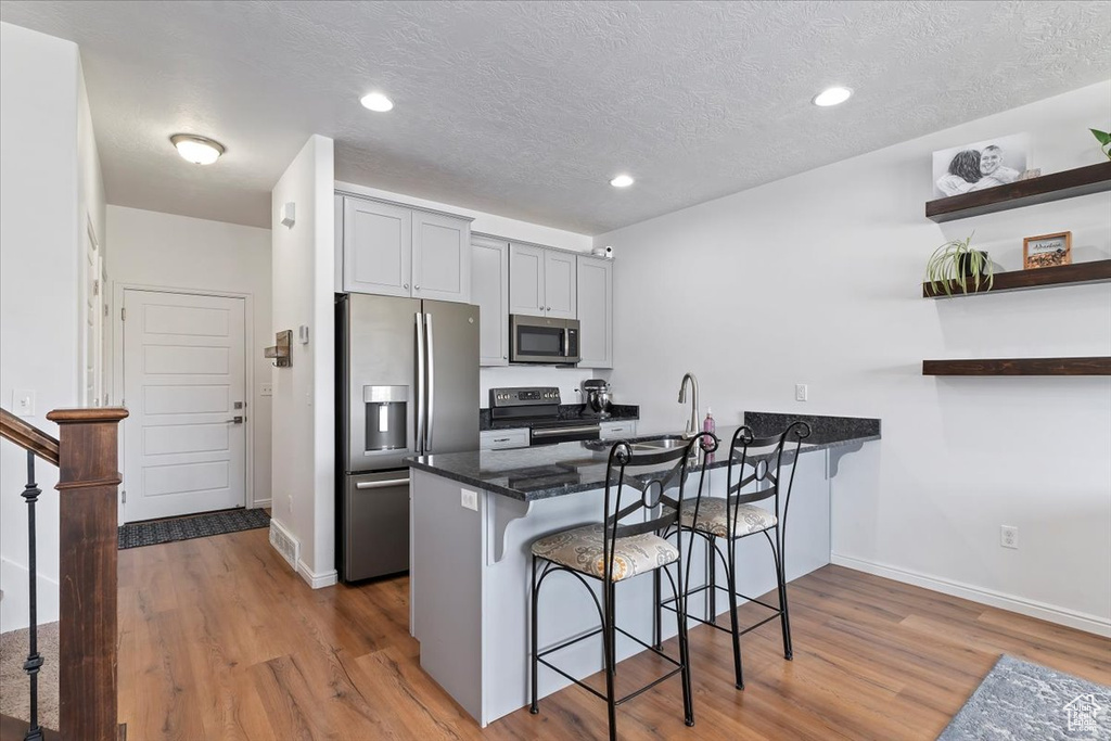 Kitchen with appliances with stainless steel finishes, a kitchen bar, a peninsula, wood finished floors, and open shelves