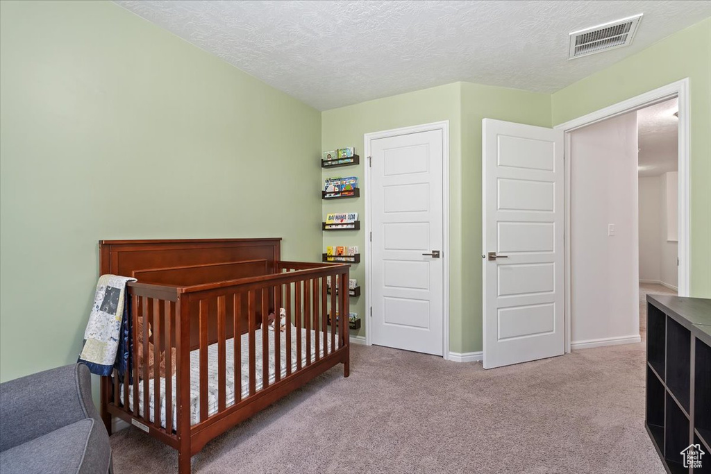 Bedroom with carpet floors, a textured ceiling, baseboards, and a nursery area