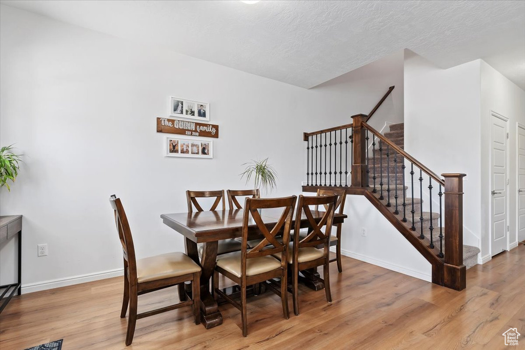 Dining area featuring light wood-style flooring, stairs, baseboards, and a textured ceiling