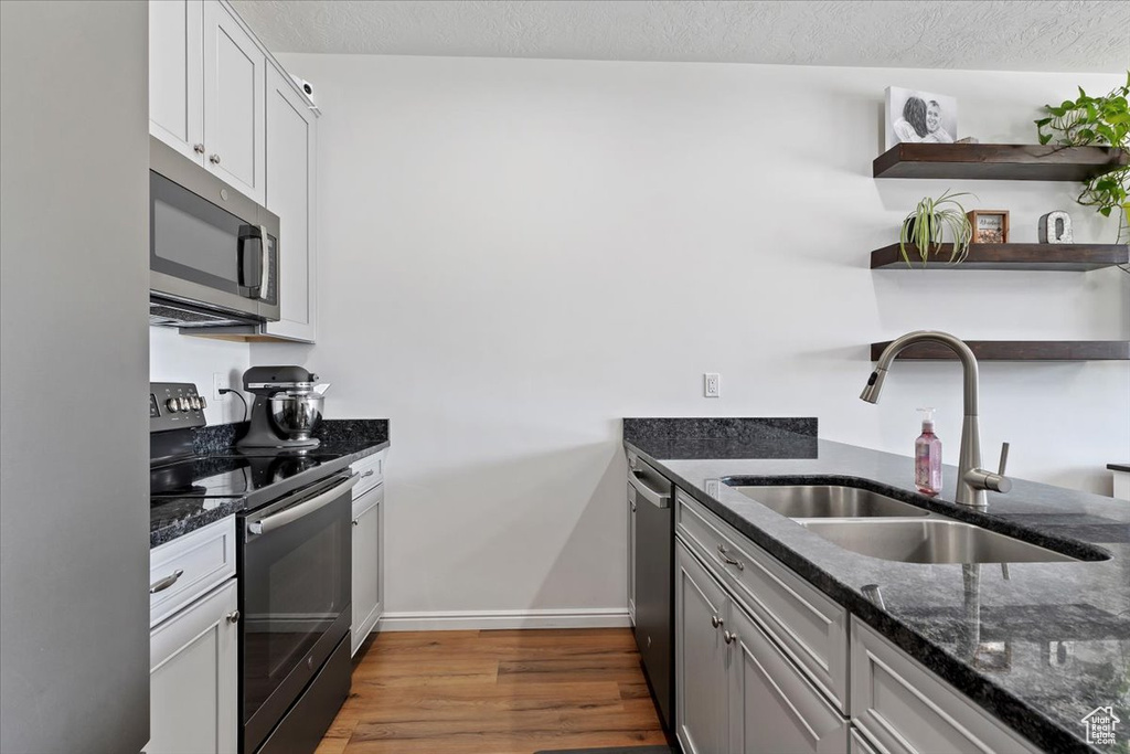 Kitchen with stainless steel appliances, a sink, open shelves, wood finished floors, and dark stone countertops