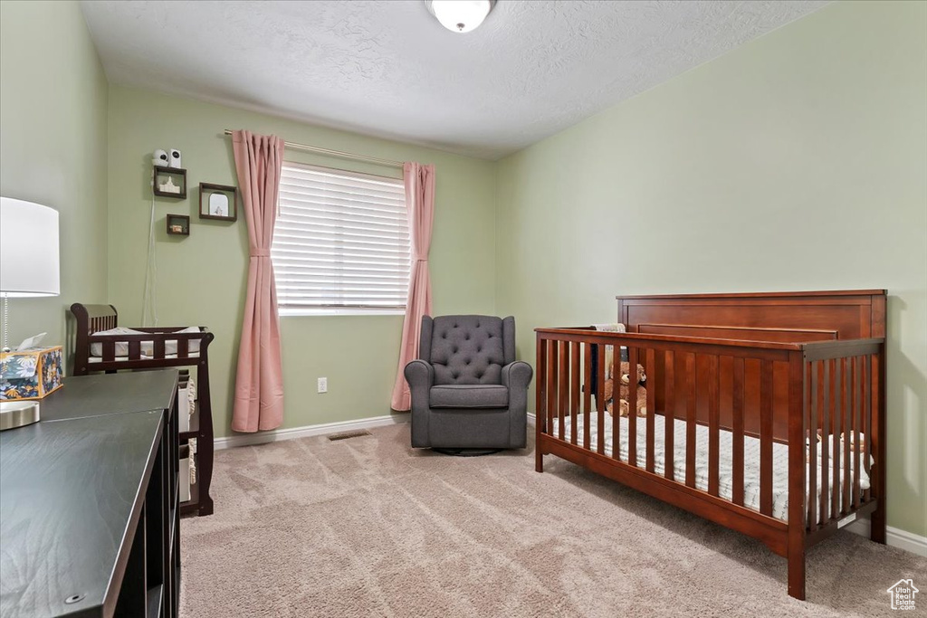 Carpeted bedroom with baseboards, a textured ceiling, and a crib