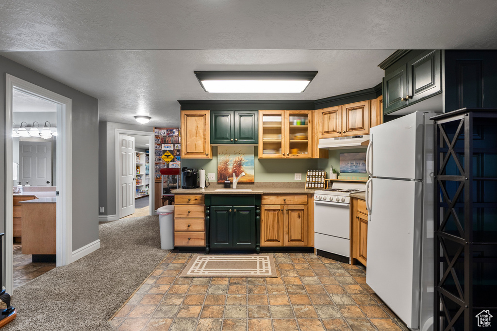 Kitchen featuring white appliances, under cabinet range hood, a sink, baseboards, and light stone finish floors