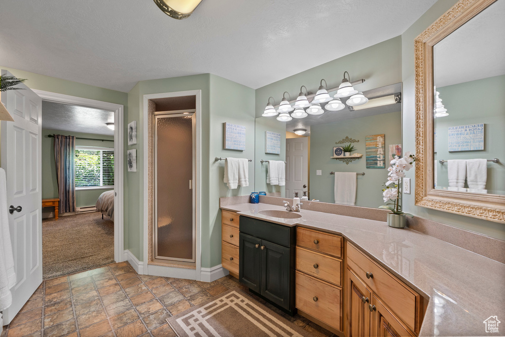 Ensuite bathroom featuring vanity, a shower stall, baseboards, and stone finish flooring