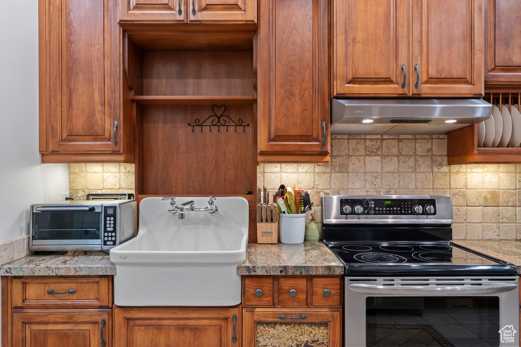 Kitchen with electric stove, under cabinet range hood, a sink, and backsplash