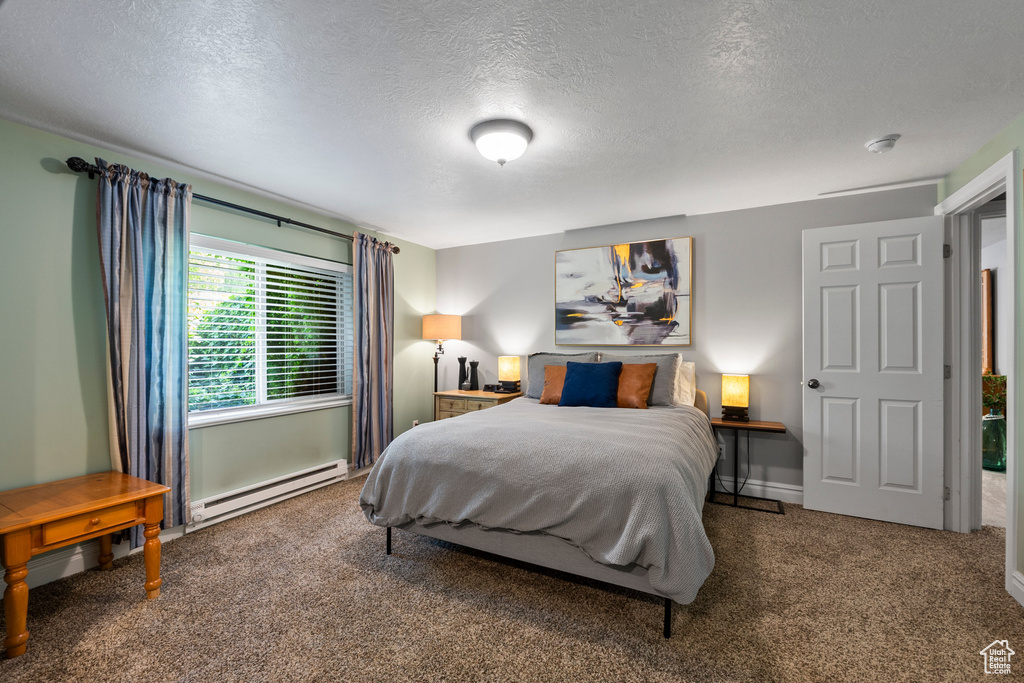 Carpeted bedroom with a baseboard heating unit and a textured ceiling