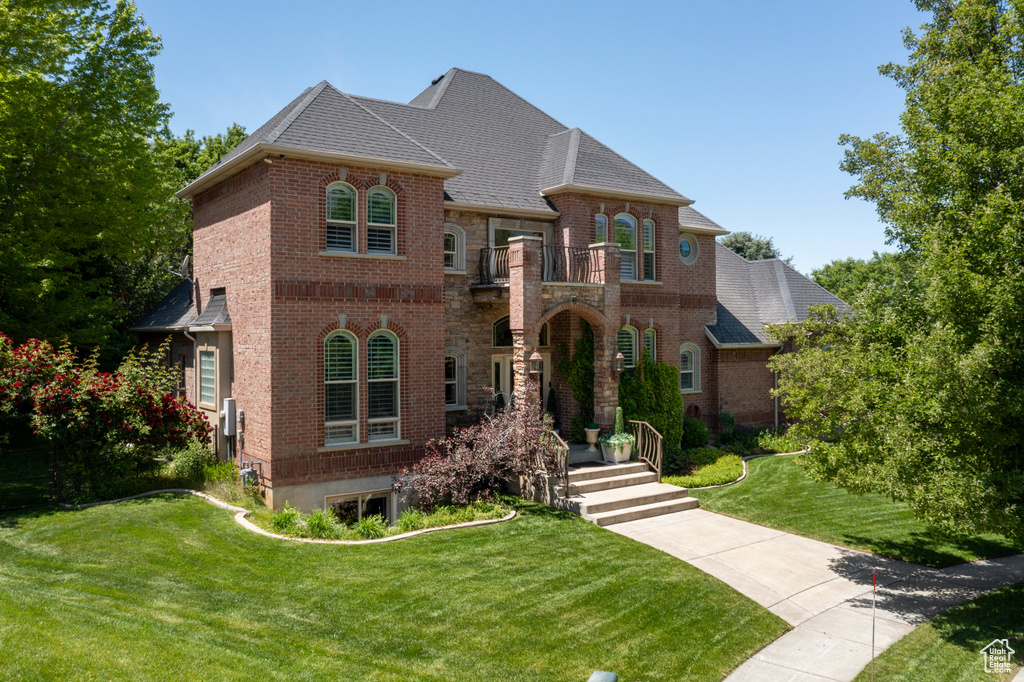 View of front of house with a balcony, brick siding, a front yard, and roof with shingles