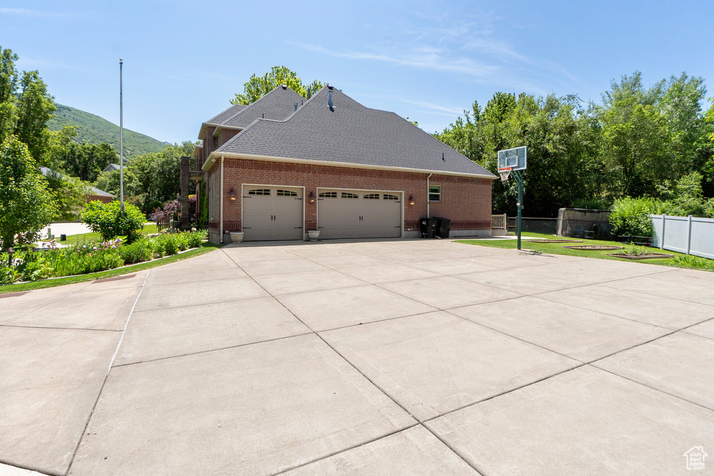 View of home\\\'s exterior with an attached garage, brick siding, concrete driveway, a shingled roof, and a mountain view