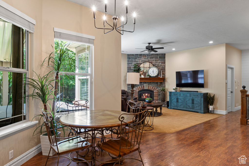 Dining area with wood finished floors, ceiling fan, baseboards, a large fireplace, and a chandelier