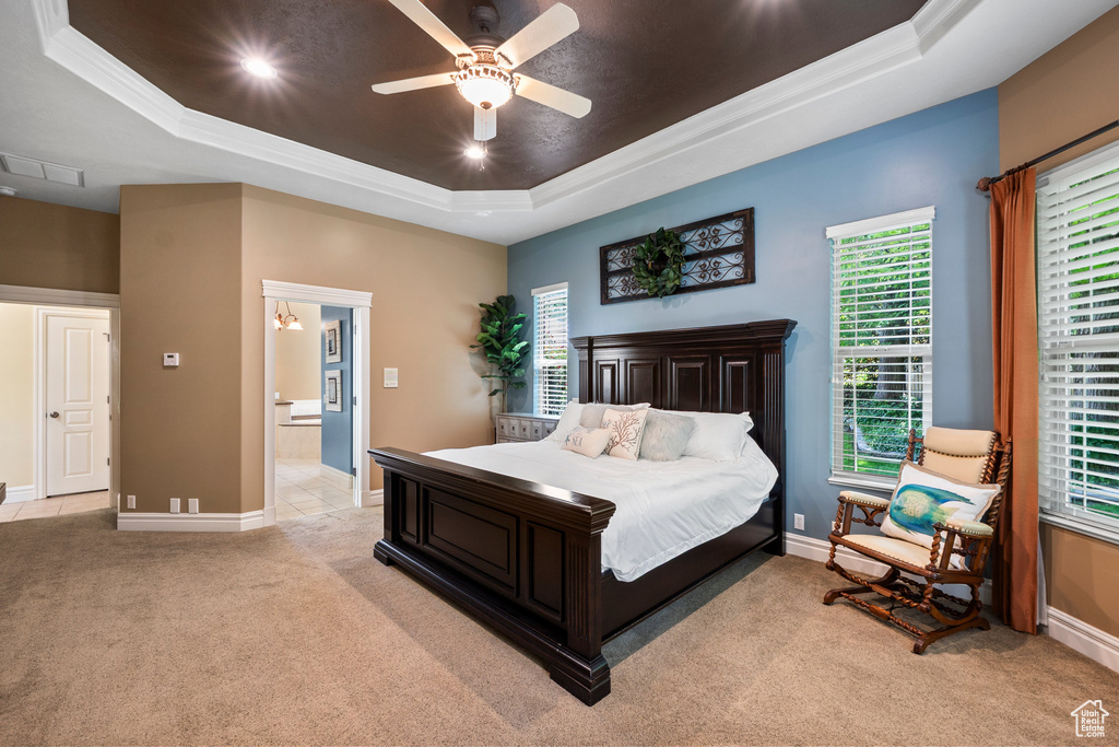 Bedroom featuring a tray ceiling, light carpet, multiple windows, crown molding, and baseboards