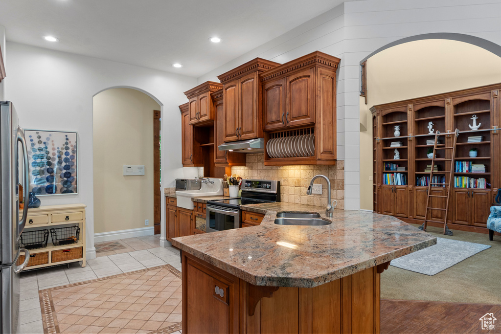 Kitchen featuring stainless steel appliances, a sink, under cabinet range hood, a peninsula, and arched walkways