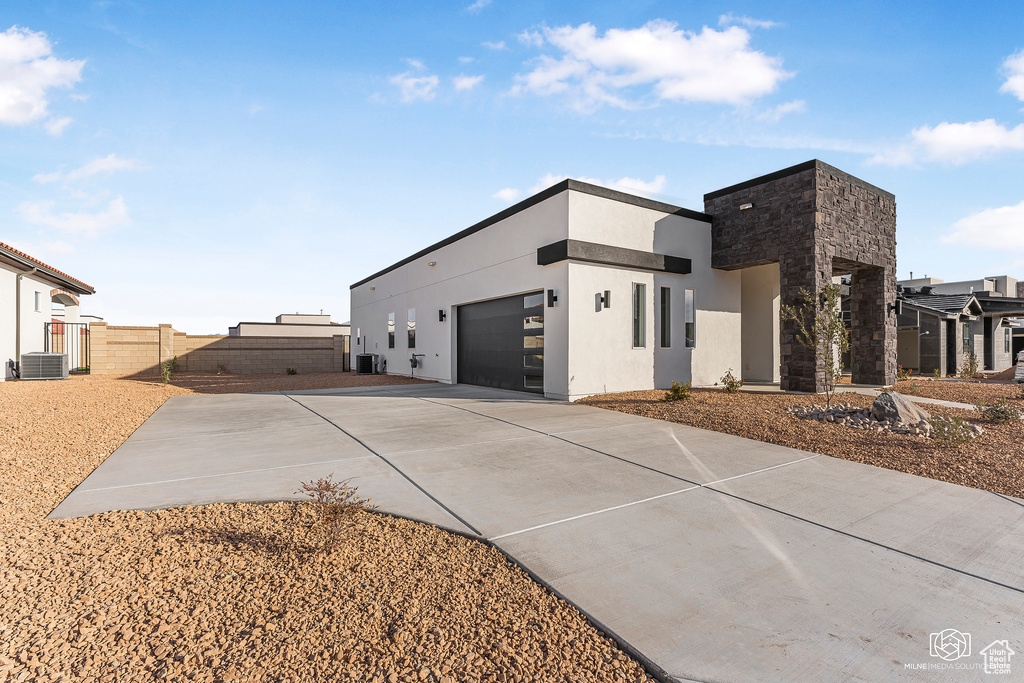 View of side of property with central air condition unit, an attached garage, driveway, and stucco siding