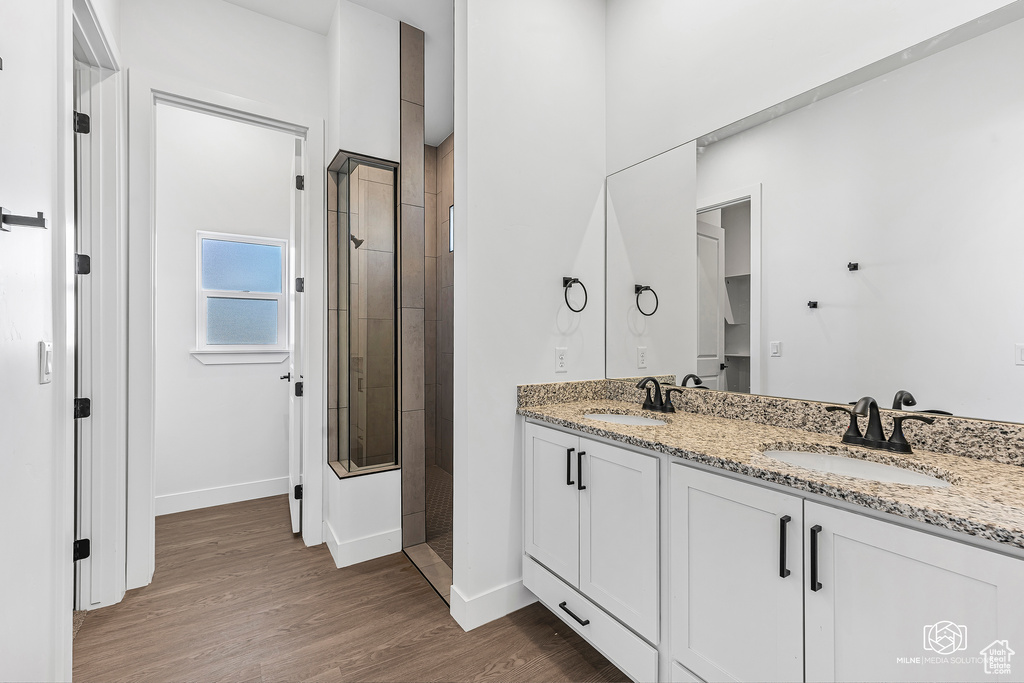 Bathroom with a stall shower, baseboards, double vanity, and wood finished floors
