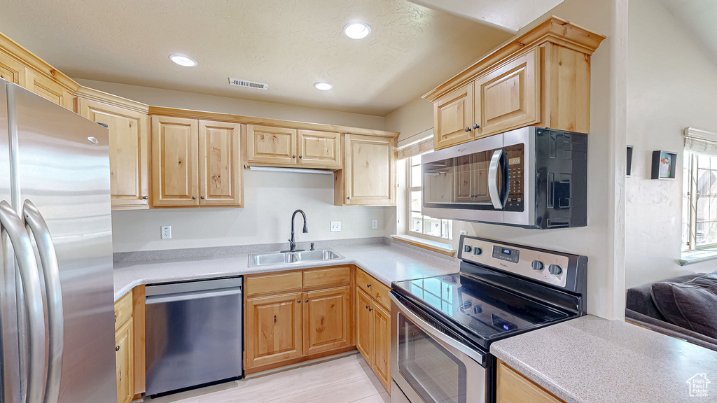 Kitchen with stainless steel appliances, a sink, light brown cabinetry, light countertops, and recessed lighting