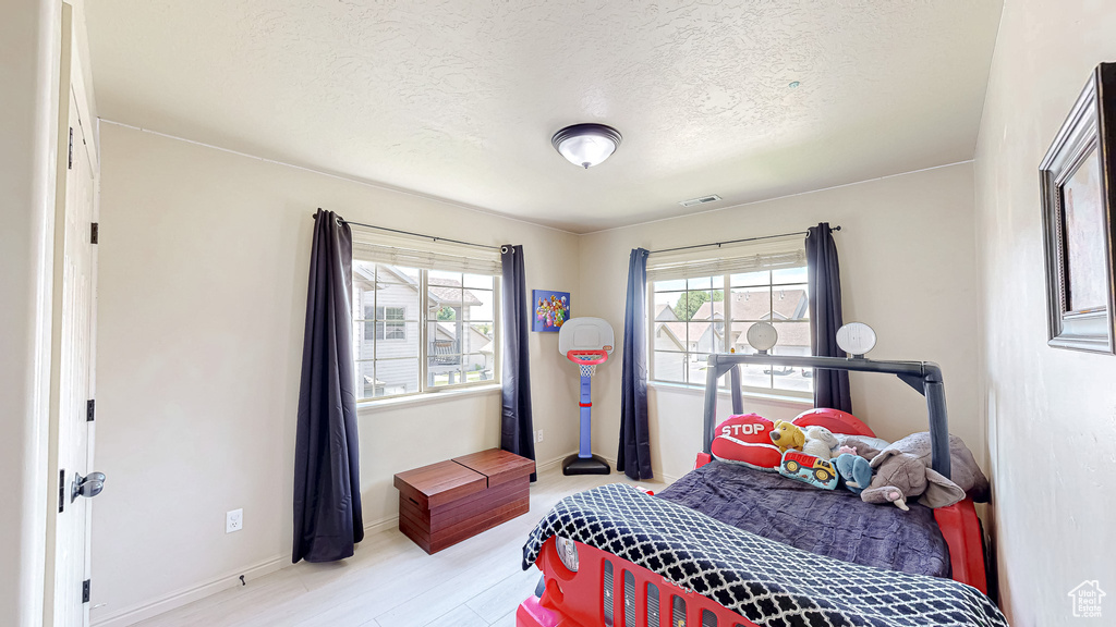Bedroom with a textured ceiling, light wood-style floors, and baseboards