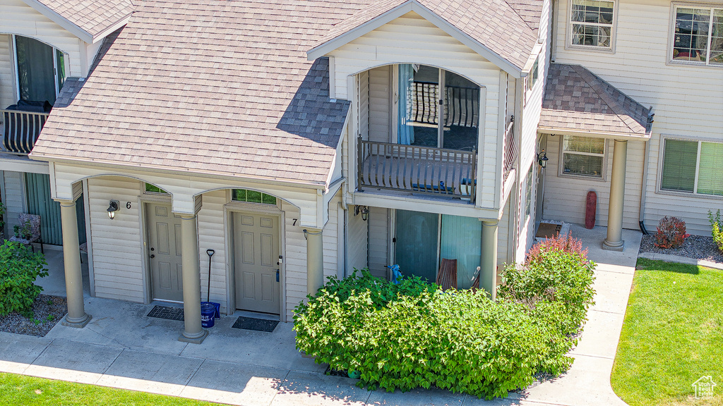View of exterior entry featuring a shingled roof and a balcony