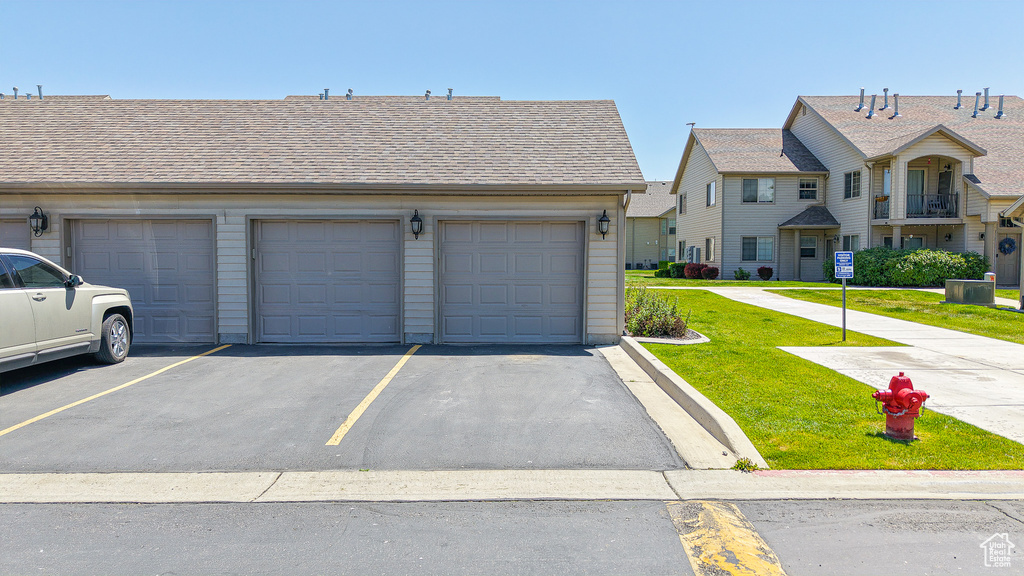 View of front of house with a front lawn, community garages, and roof with shingles