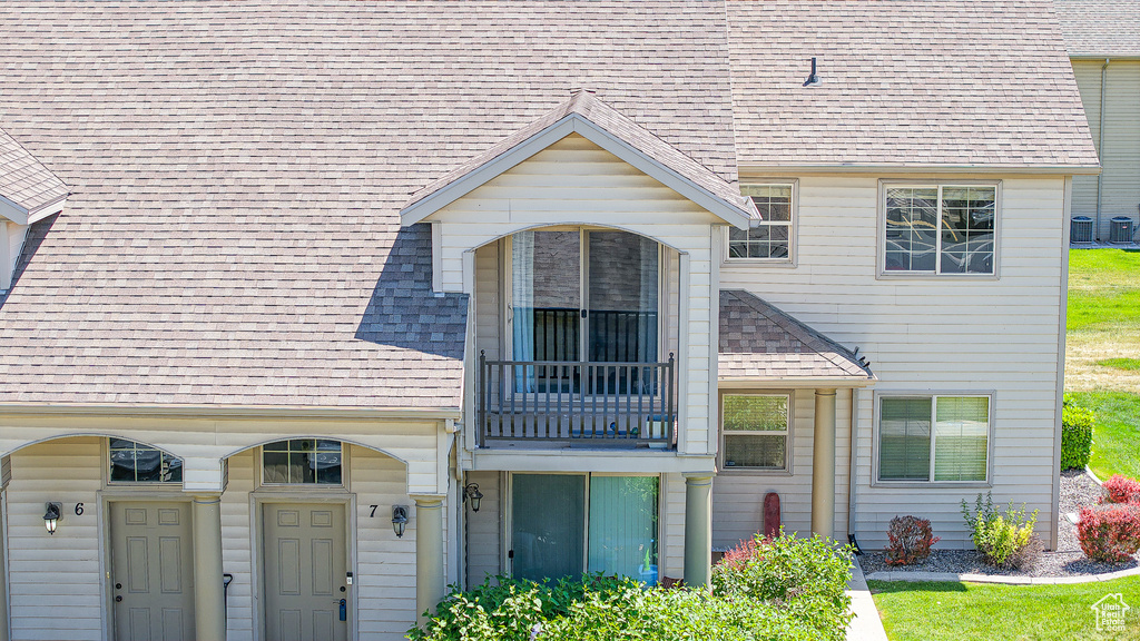 View of front facade featuring a balcony, roof with shingles, and central air condition unit