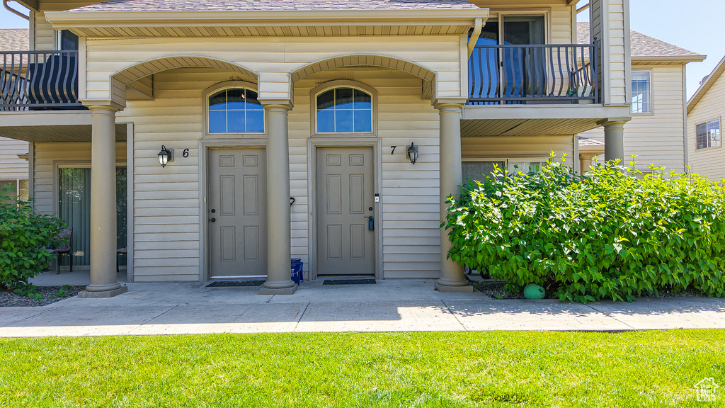 View of exterior entry featuring a balcony, roof with shingles, and a yard
