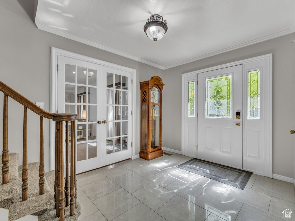 Foyer entrance featuring french doors, baseboards, crown molding, and stairway