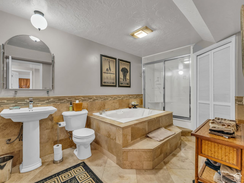 Bathroom featuring a garden tub, a stall shower, toilet, tile patterned floors, and a textured ceiling