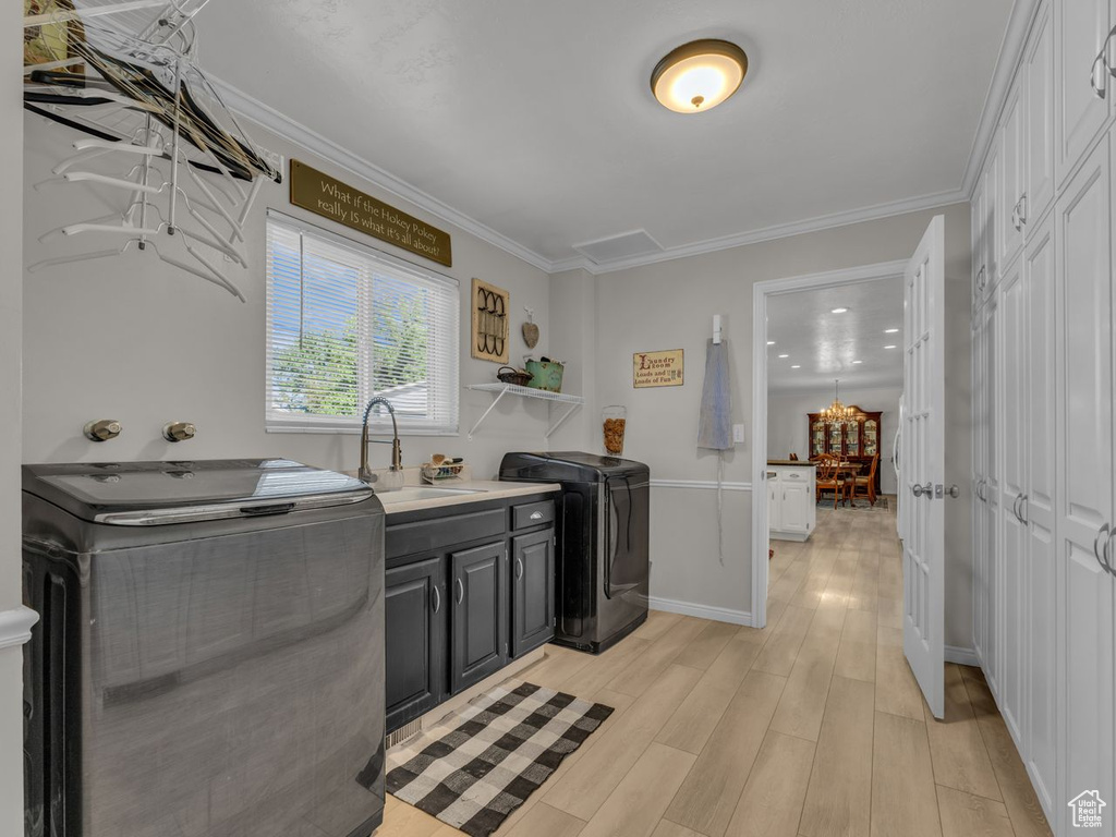 Laundry area with cabinet space, washer and clothes dryer, light wood-style floors, ornamental molding, and a chandelier