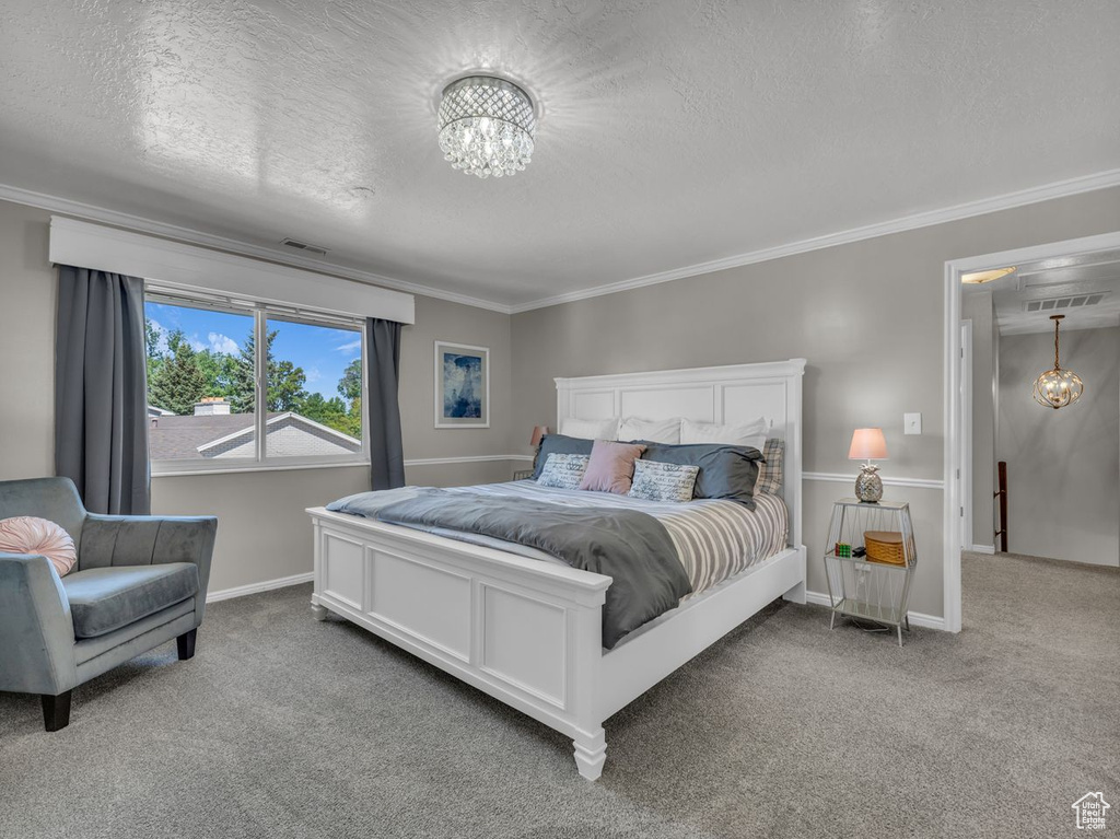 Carpeted bedroom featuring a chandelier, a textured ceiling, crown molding, and baseboards