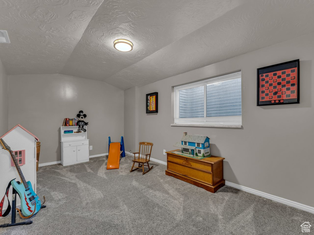 Recreation room with lofted ceiling, a textured ceiling, carpet, and baseboards