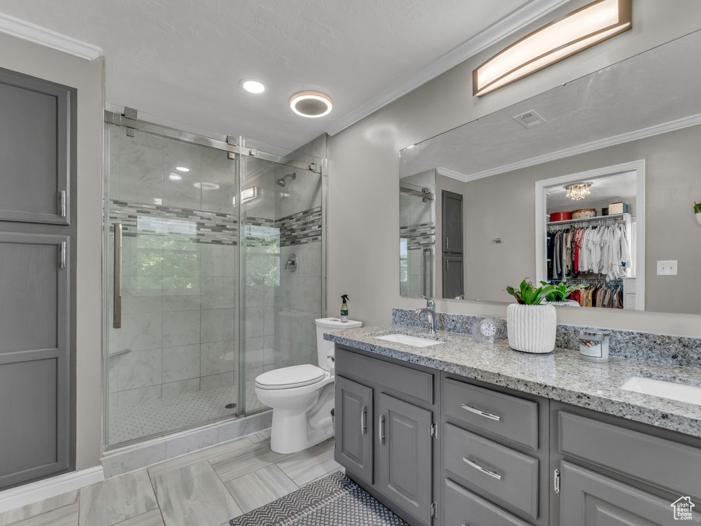 Full bath with double vanity, a shower stall, ornamental molding, a walk in closet, and toilet