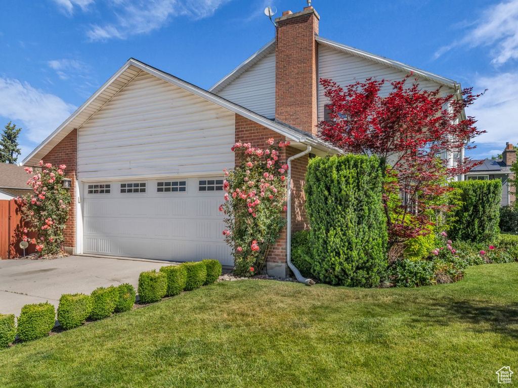 View of front of property featuring a chimney, concrete driveway, brick siding, a garage, and a front yard