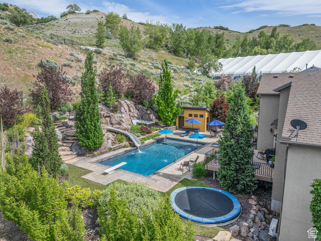 Swimming pool featuring a trampoline, a water slide, a diving board, a deck with mountain view, and an outdoor structure