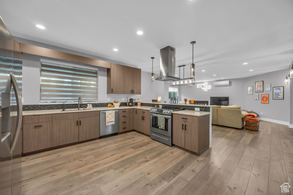 Kitchen featuring appliances with stainless steel finishes, island exhaust hood, open floor plan, a peninsula, and a wall unit AC