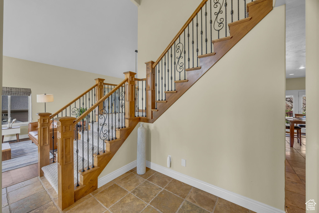 Staircase with baseboards, stone tile floors, and a high ceiling