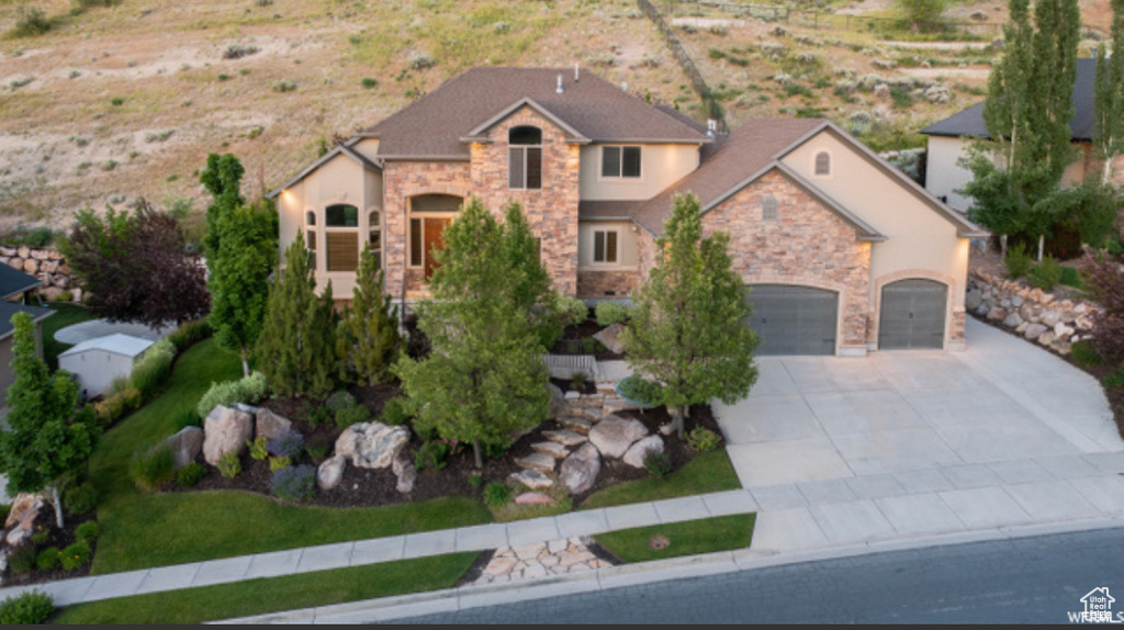View of front facade with stone siding, driveway, an attached garage, and stucco siding
