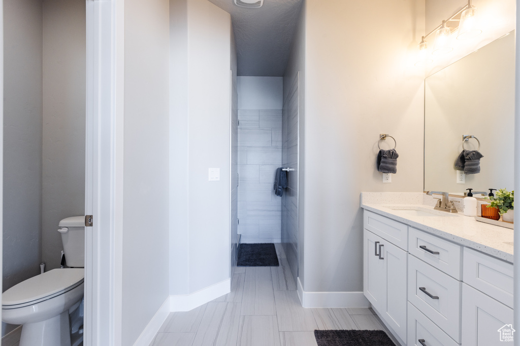 Bathroom featuring vanity, toilet, baseboards, and a tile shower