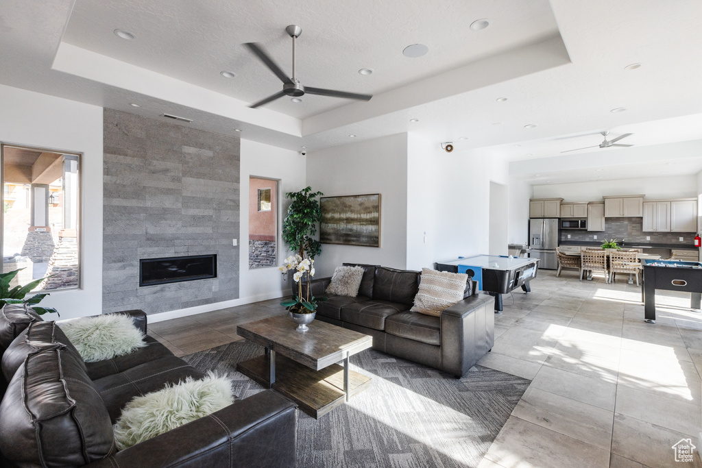 Living room with a ceiling fan, a tray ceiling, recessed lighting, and a tiled fireplace