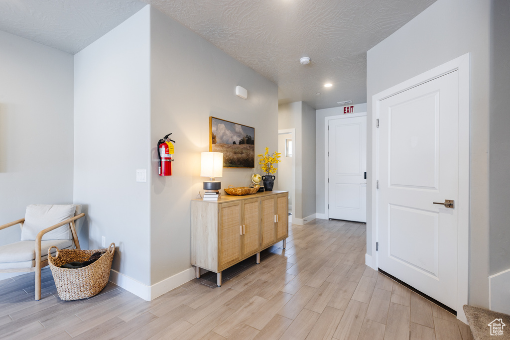 Hallway featuring light wood finished floors, baseboards, recessed lighting, and a textured ceiling