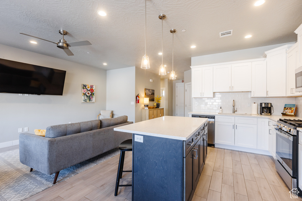 Kitchen featuring appliances with stainless steel finishes, a sink, open floor plan, white cabinetry, and a kitchen bar