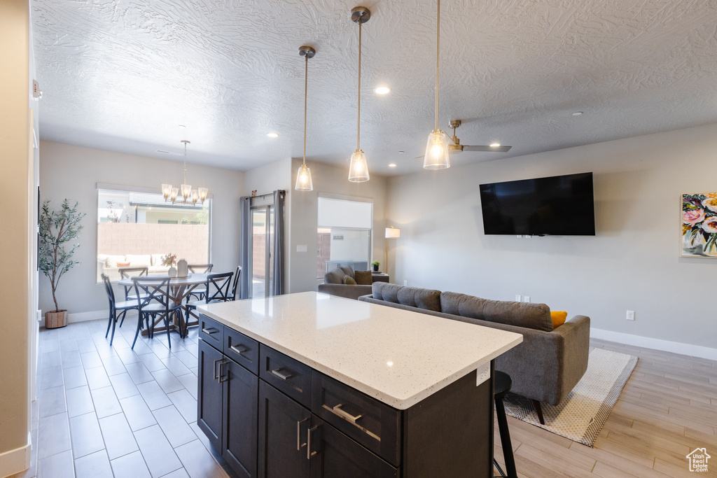 Kitchen featuring baseboards, open floor plan, a textured ceiling, a center island, and recessed lighting