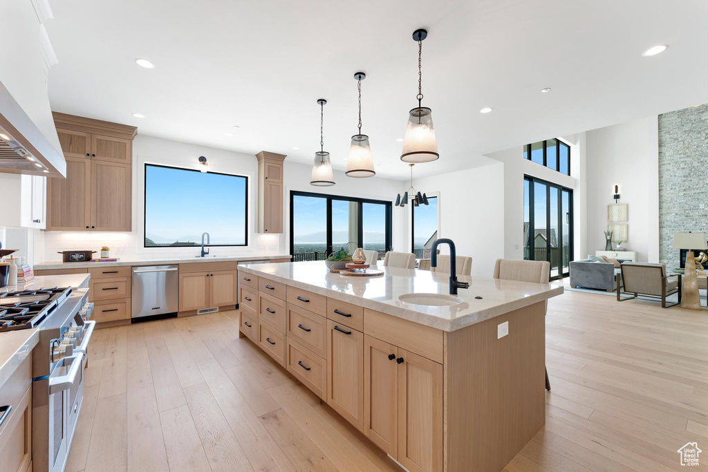 Kitchen featuring stainless steel appliances, light brown cabinetry, a sink, custom range hood, and a center island with sink