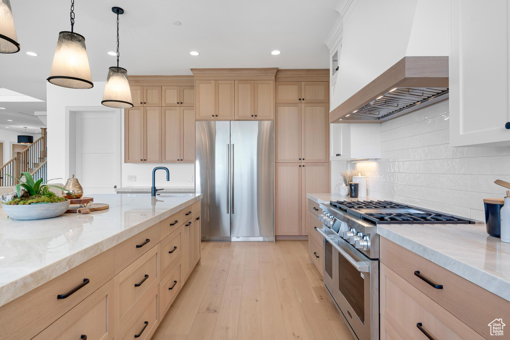 Kitchen with appliances with stainless steel finishes, wall chimney range hood, light brown cabinetry, light stone countertops, and recessed lighting