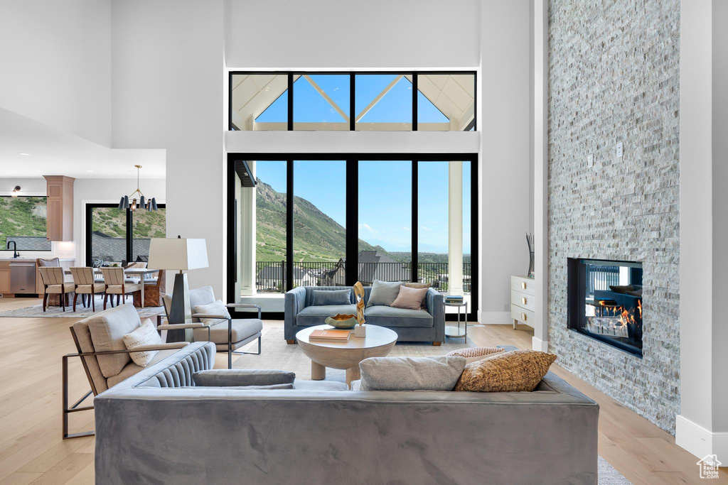 Living room featuring a high ceiling, light wood-style floors, a stone fireplace, baseboards, and a mountain view