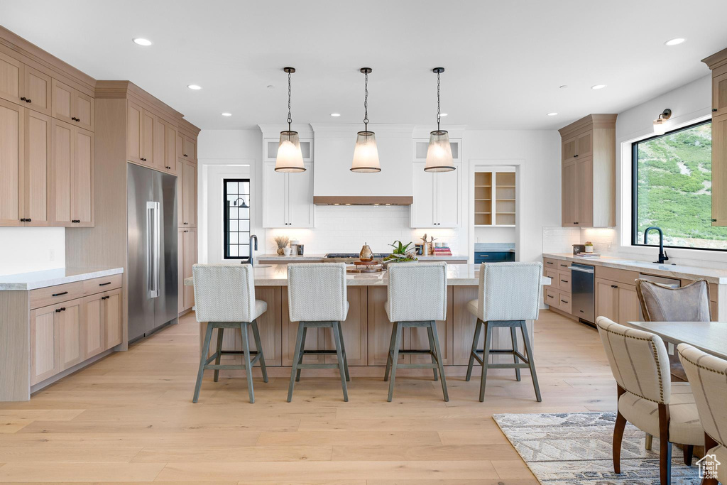 Kitchen featuring stainless steel appliances, custom range hood, decorative backsplash, recessed lighting, and light countertops