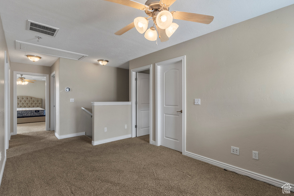 Carpeted spare room with attic access, a ceiling fan, and baseboards