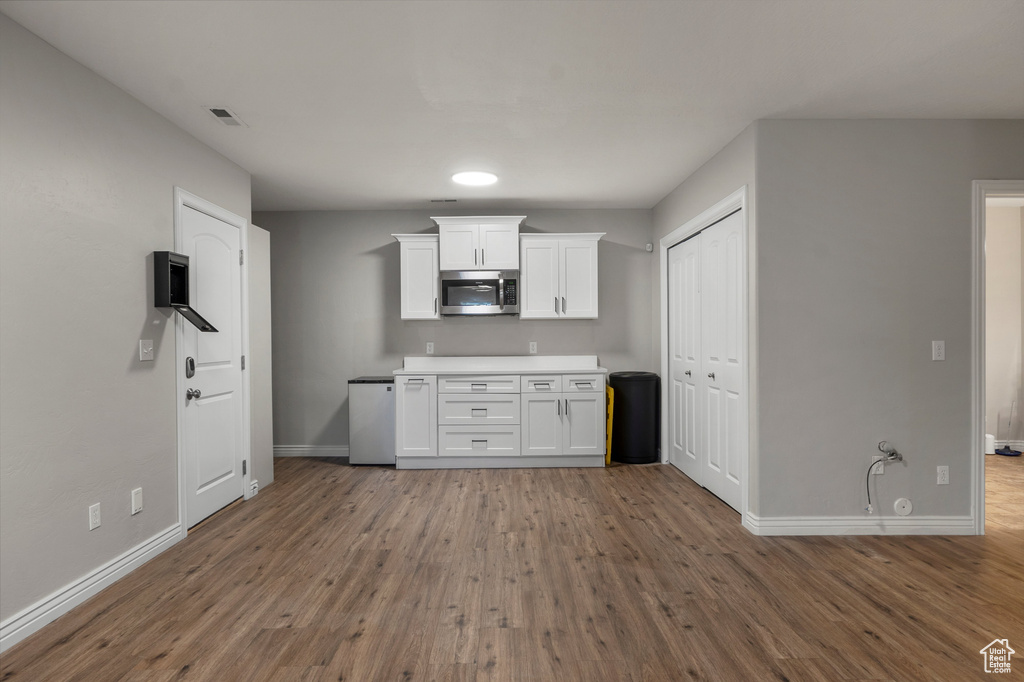 Kitchen featuring stainless steel microwave, baseboards, white cabinetry, wood finished floors, and light countertops