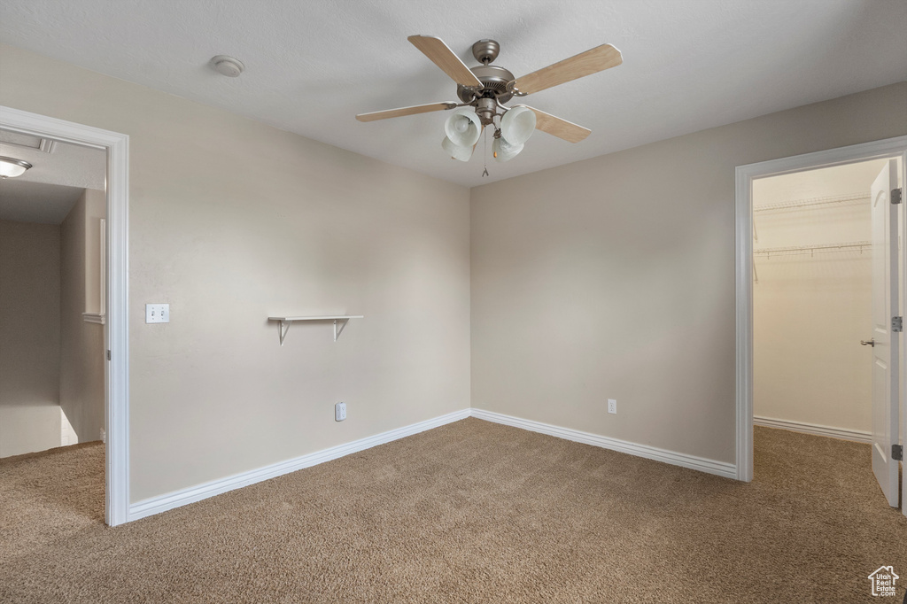 Carpeted empty room featuring ceiling fan, baseboards, and a smoke detector