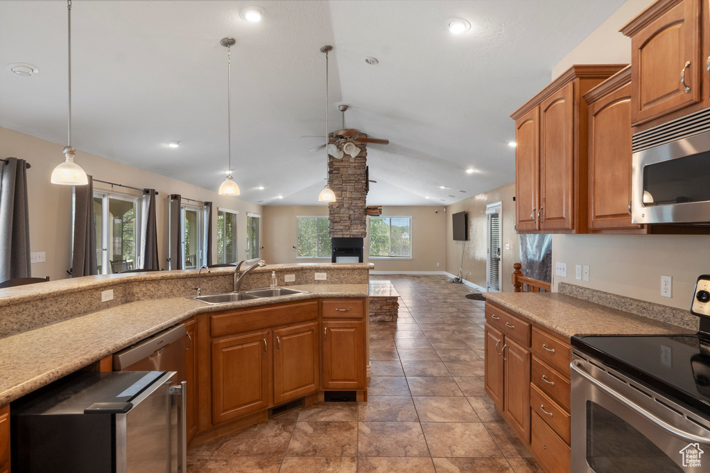 Kitchen with appliances with stainless steel finishes, a sink, vaulted ceiling, ceiling fan, and brown cabinetry