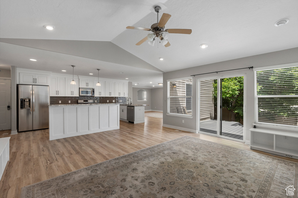 Kitchen with stainless steel appliances, open floor plan, a kitchen island, lofted ceiling, and white cabinets