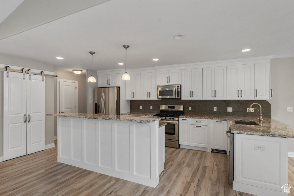 Kitchen with appliances with stainless steel finishes, a sink, white cabinetry, light wood-style flooring, and backsplash