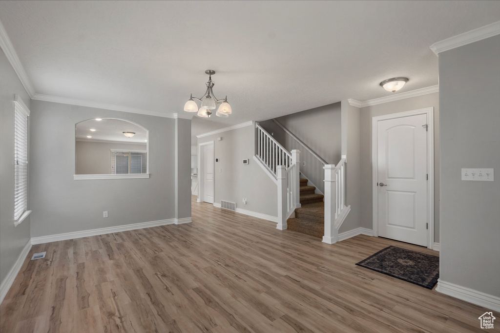 Foyer with a chandelier, wood finished floors, stairs, baseboards, and crown molding
